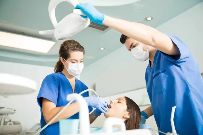 Dentist Treating Patient With Dental Tool While Male Colleague Adjusting Light Clinic X - National Dental Assisting Examination Board study guide